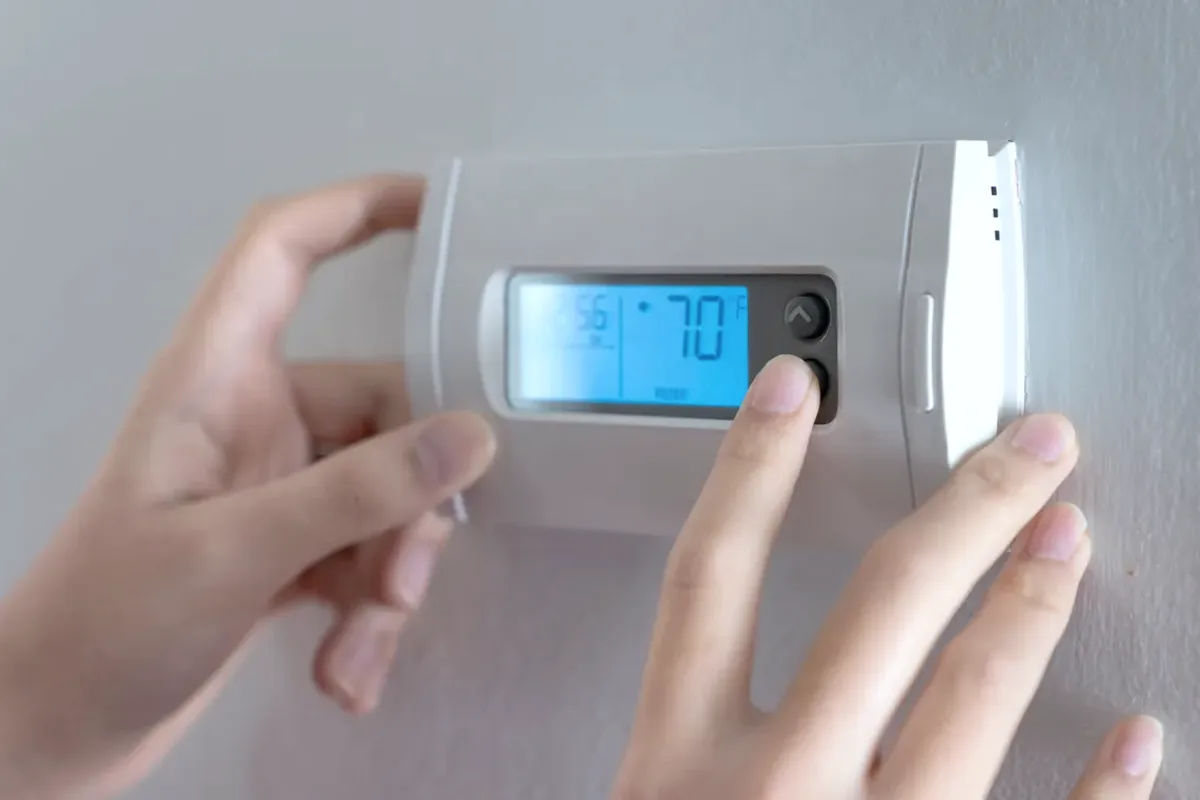 Hands adjusting a digital wall thermostat